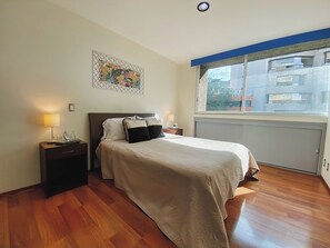 A hotel room with a bed, bedside tables, a window, and a painting on the wall.