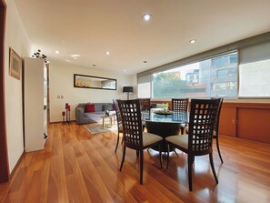 A modern living room with a dining area, wooden flooring, a sofa, a coffee table, and a large window.