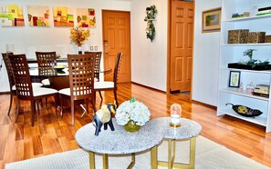 Uma área de refeições com uma mesa de madeira e cadeiras, uma pequena mesa redonda com uma vela e uma estante com objetos decorativos.