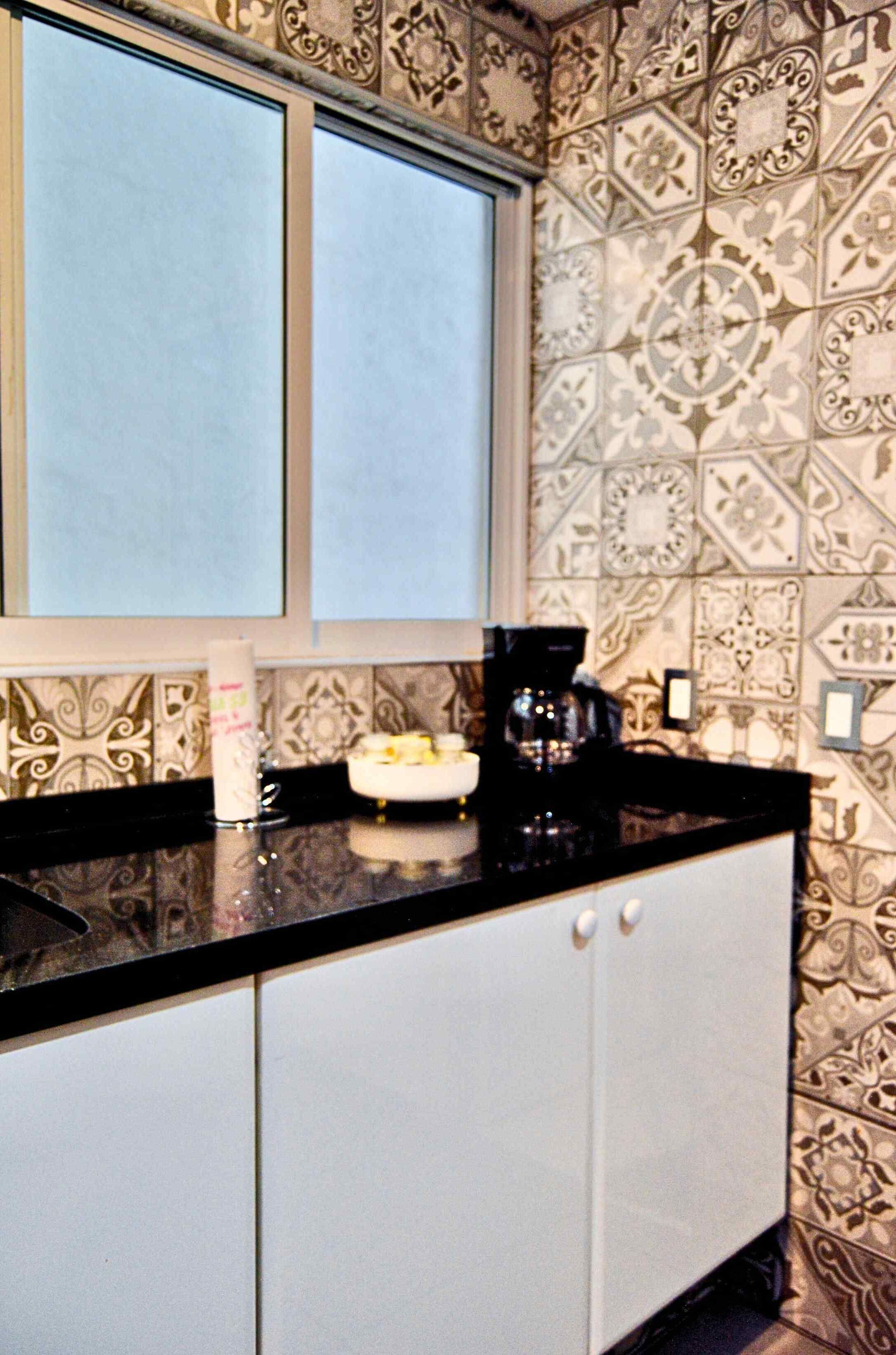 Una cocina con papel tapiz estampado, una encimera negra, una cafetera y un armario blanco.