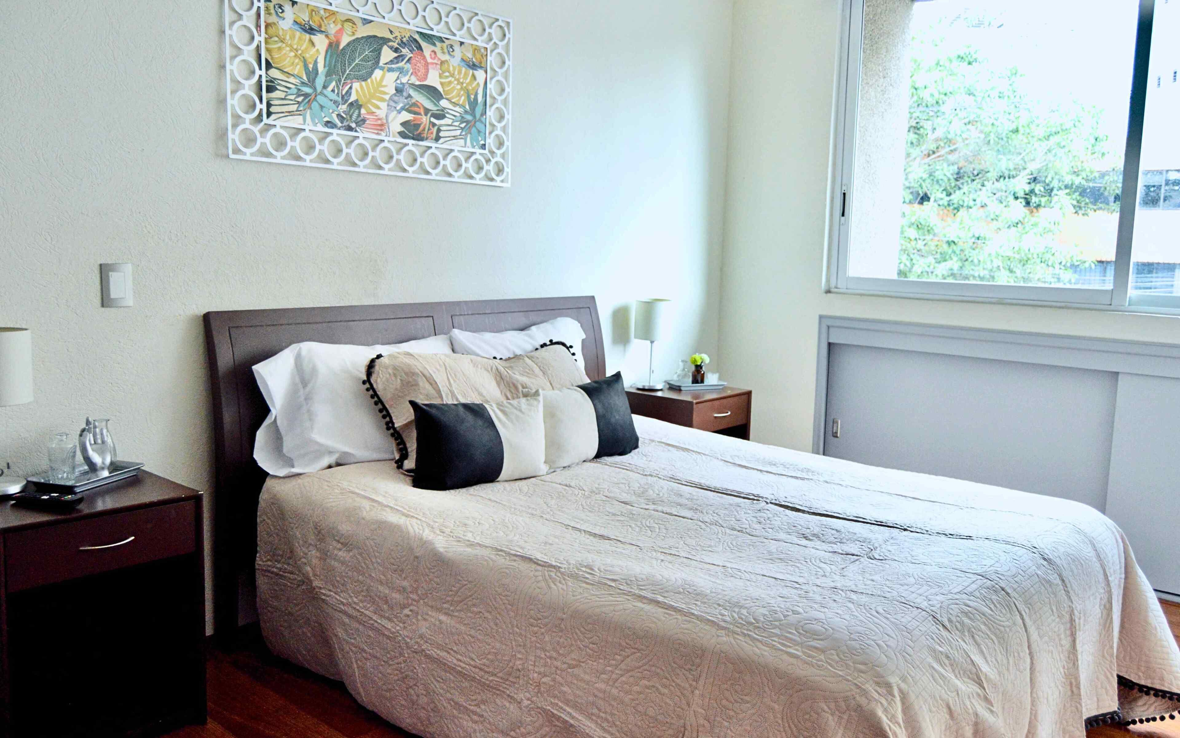 Un letto rifatto con una coperta a motivi, un comodino con una lampada e un elemento decorativo a parete.