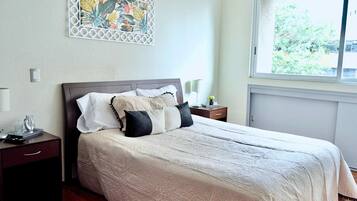 Un letto rifatto con una coperta a motivi, un comodino con una lampada e un elemento decorativo a parete.