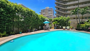 Piscina cercada por vegetação exuberante e um edifício alto ao fundo.