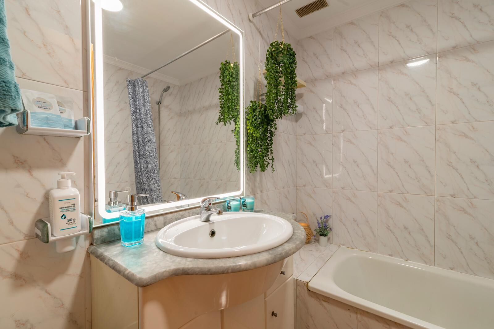 Un baño con lavamanos de mármol, un espejo grande, ducha y plantas verdes.