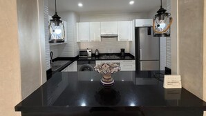 A modern kitchen with black countertops, white cabinets, and two pendant lights. - Superb apartment at the marina (Agadir)