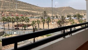 A balcony with a view of a hilly landscape, palm trees, and a road with cars. - Superb apartment at the marina (Agadir)