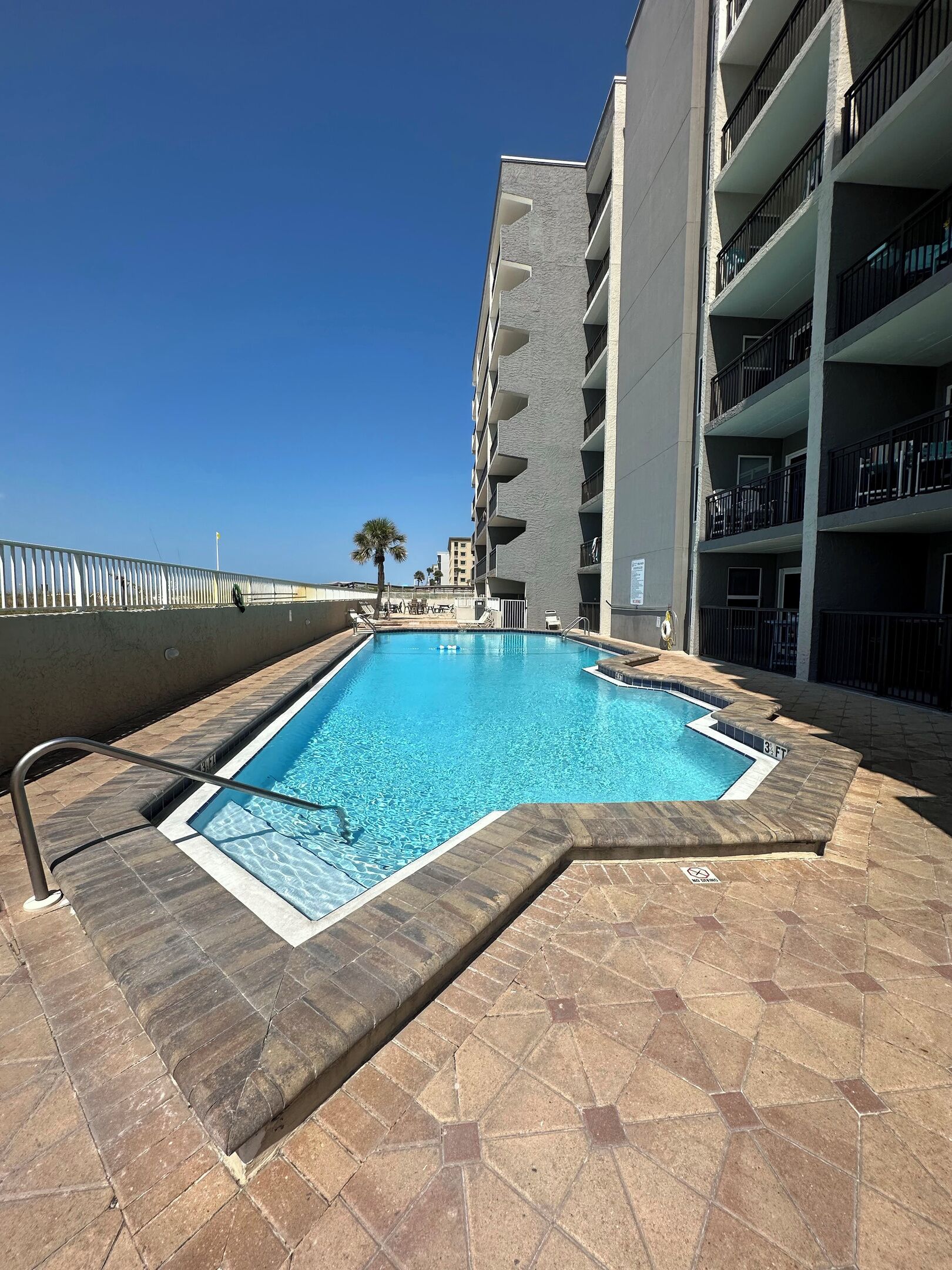A swimming pool with a tiled deck, surrounded by a high-rise building with balconies.