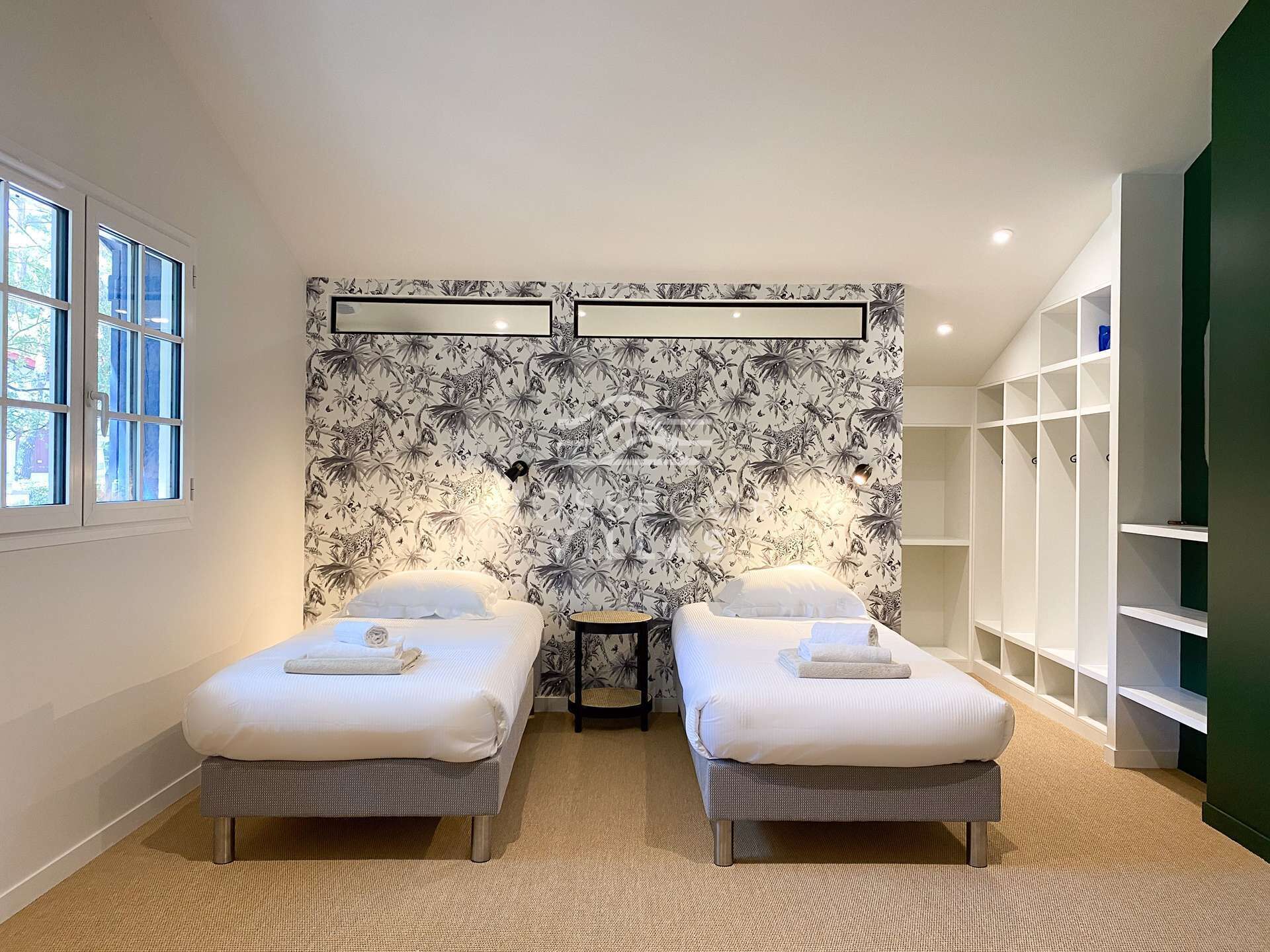 Un dormitorio moderno con dos camas individuales, un ventanal grande, un papel tapiz decorativo y espacio de almacenamiento integrado.