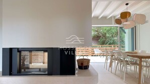 A modern interior with a fireplace, dining area, and large windows offering a view of the outdoors.