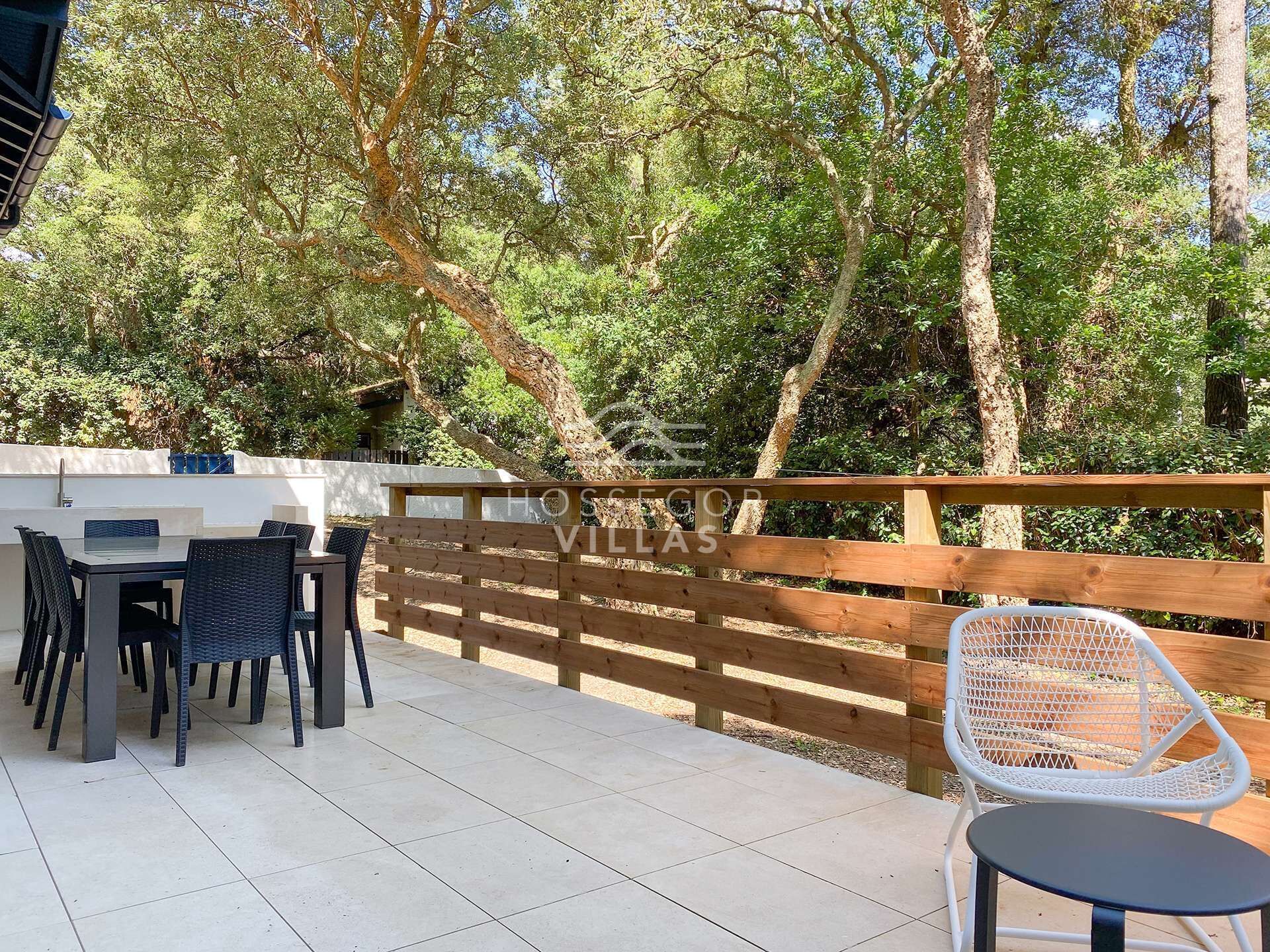 Une terrasse extérieure avec une table et des chaises, entourée d’une clôture en bois et d’arbres.