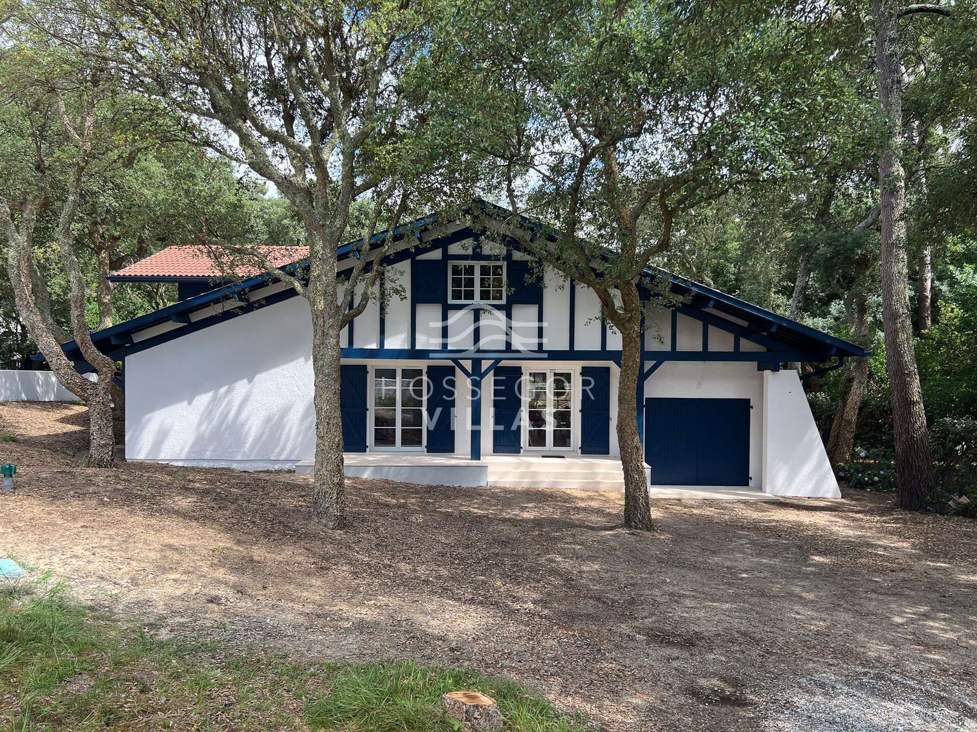A traditional half-timbered house with a white facade and blue accents, surrounded by trees.