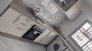Cozinha com armários brancos, fogão, máquina de lavar e janela com vista para edifícios.