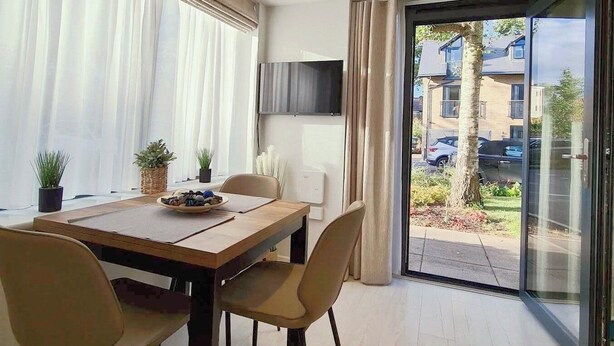 Un comedor moderno con una mesa de madera, cuatro sillas y un televisor montado en la pared.