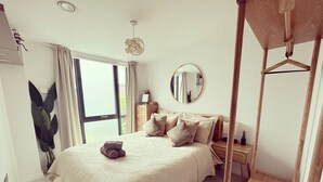 Un dormitorio con una cama grande, una mesita de noche, una lámpara colgante y una ventana con cortinas.