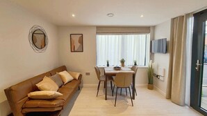 Una sala moderna con sofá, mesa de comedor, sillas, televisor y un ventanal con cortinas.