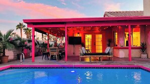 A poolside area with a covered seating area, a pool, and a building with a red roof. - Welcome to The Pink Cabana, where modern Moroccan meets luxe desert vibes. (Indio)