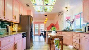 A kitchen with pink cabinets, a refrigerator, a wooden table, and a patterned rug. - Welcome to The Pink Cabana, where modern Moroccan meets luxe desert vibes. (Indio)