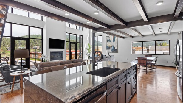 A modern kitchen with a large island, wooden flooring, and large windows offering views of the outdoors. - McGregor and Main Luxury Lofts (Hill City)