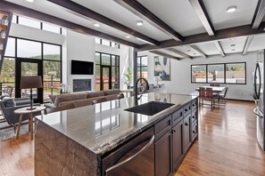 A modern kitchen with a large island, wooden flooring, and large windows offering views of the outdoors. - McGregor and Main Luxury Lofts (Hill City)