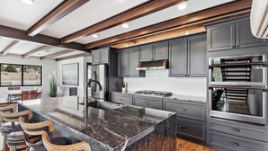 A modern kitchen with dark cabinets, stainless steel appliances, and a large island with bar stools. - McGregor and Main Luxury Lofts (Hill City)