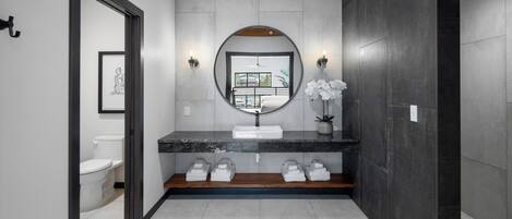 Un baño moderno con un espejo grande, un lavamanos redondo y vistas a un balcón.