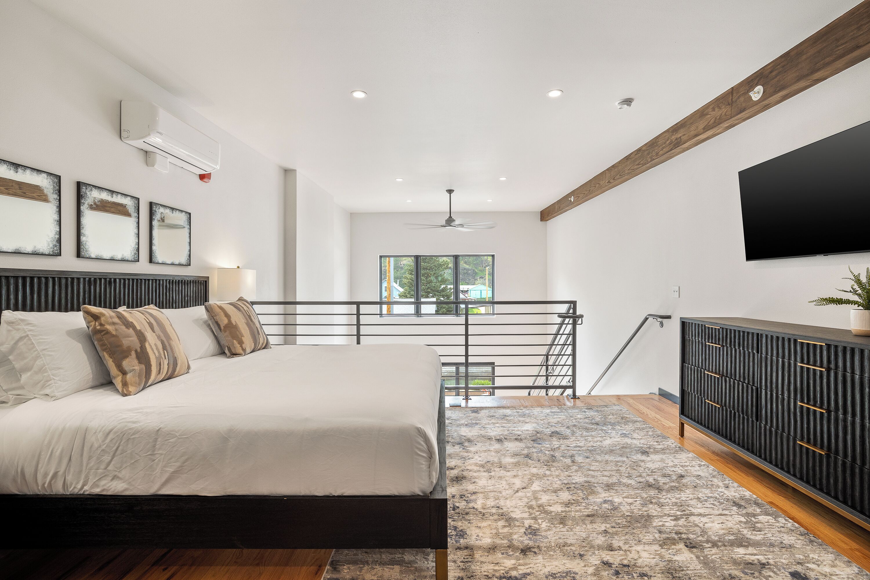 A modern bedroom with a bed, a large window, a TV, and a staircase.