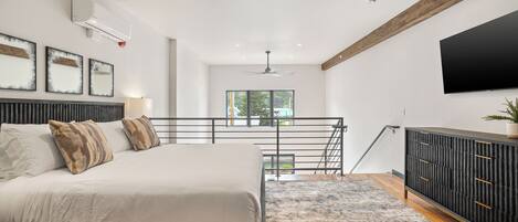 A modern bedroom with a bed, a large window, a TV, and a staircase.