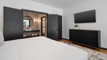Een moderne slaapkamer met een groot bed, een donkere dressoir, een flatscreen televisie en een badkamer die door een open deur zichtbaar is.