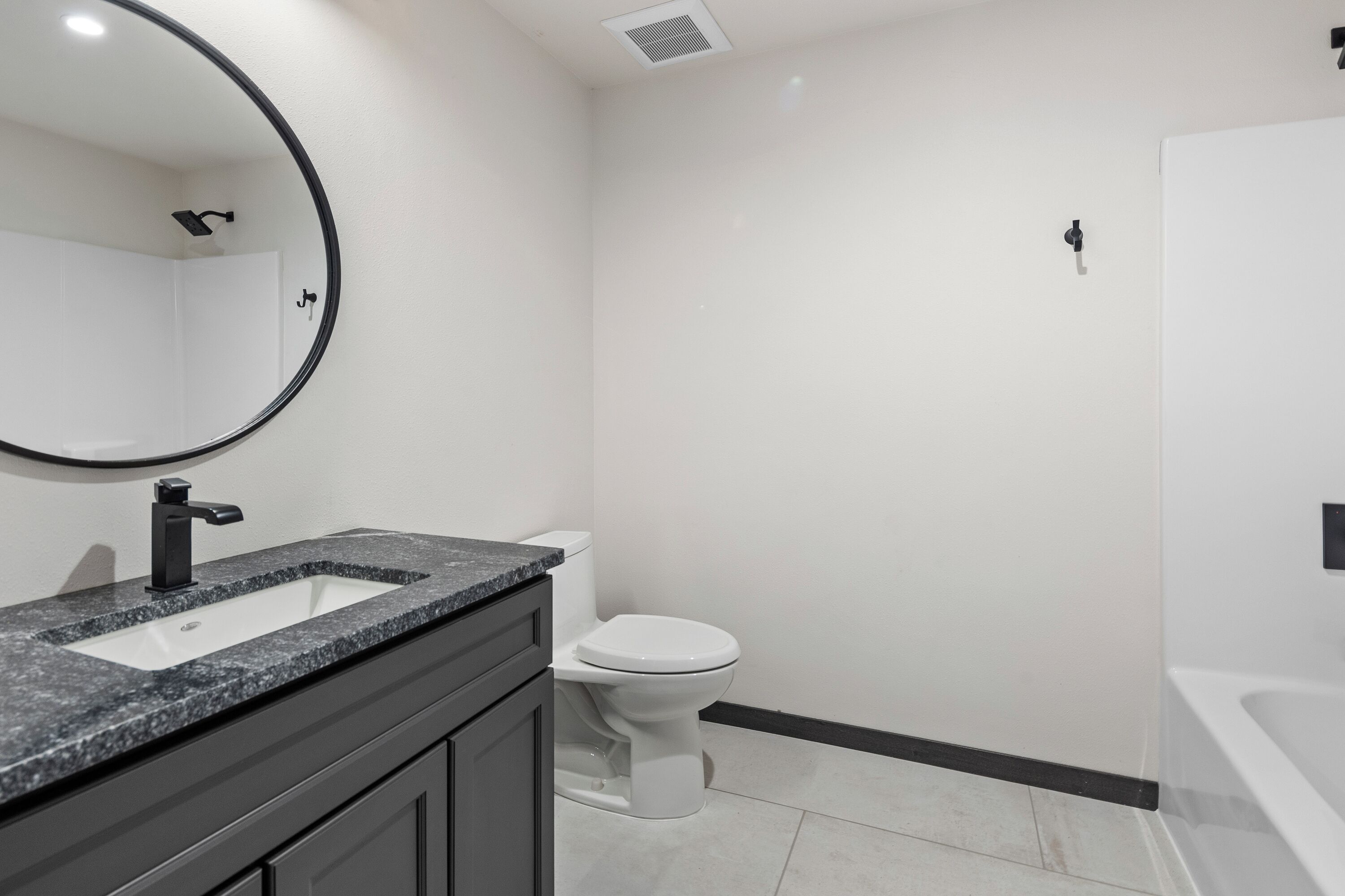 Un baño moderno con inodoro blanco, lavamanos con grifo negro y un espejo grande sobre el lavamanos.