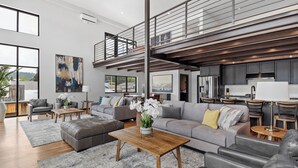 A spacious living area with a modern design, featuring a large sofa, a coffee table, and a dining area with a kitchen in the background. - McGregor and Main Luxury Lofts (Hill City)