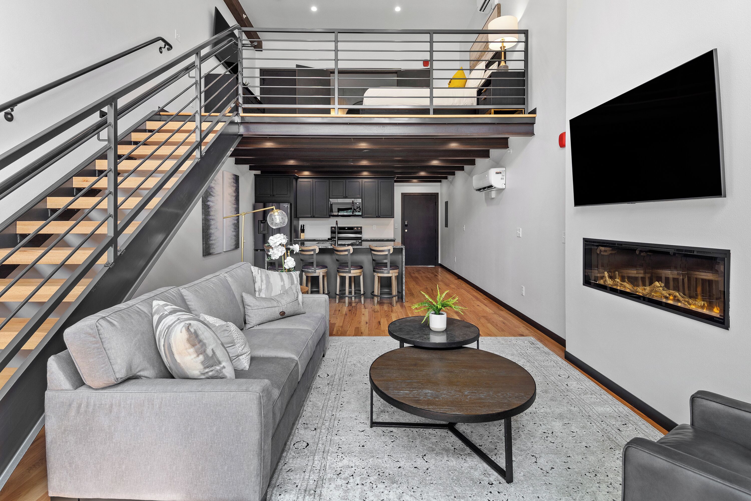 A modern living room with a grey sofa, a coffee table, and a staircase leading to a loft area.