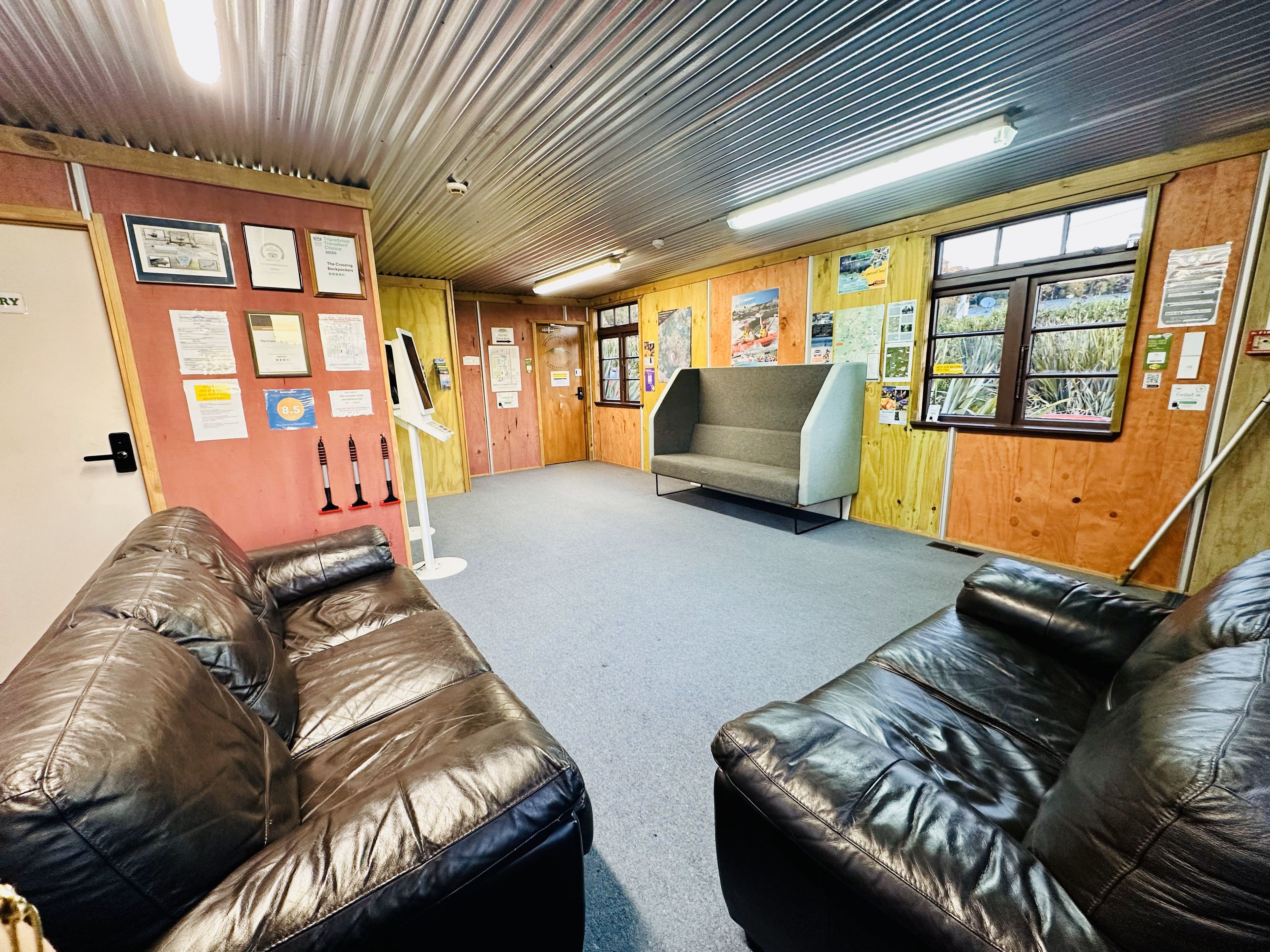 A room with a sofa, a cushioned bench, a wooden wall with various notices, and a window with a view of greenery.