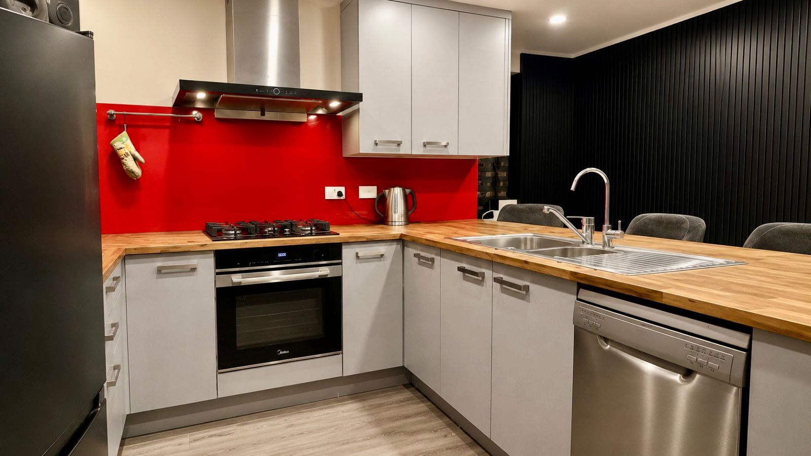 Una cocina moderna con un refrigerador de acero inoxidable, un horno empotrado, un lavavajillas y una pared de acento roja.