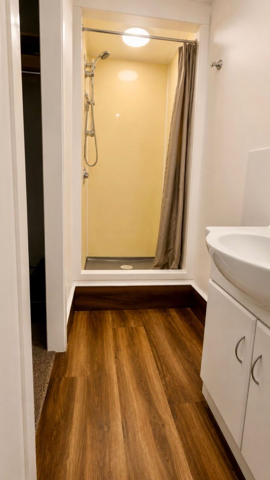 Un bagno con doccia, lavandino e pavimento in legno.