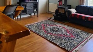 Una sala de estar acogedora con techo de madera, un sofá, un televisor, una chimenea y un comedor con mesa y sillas.