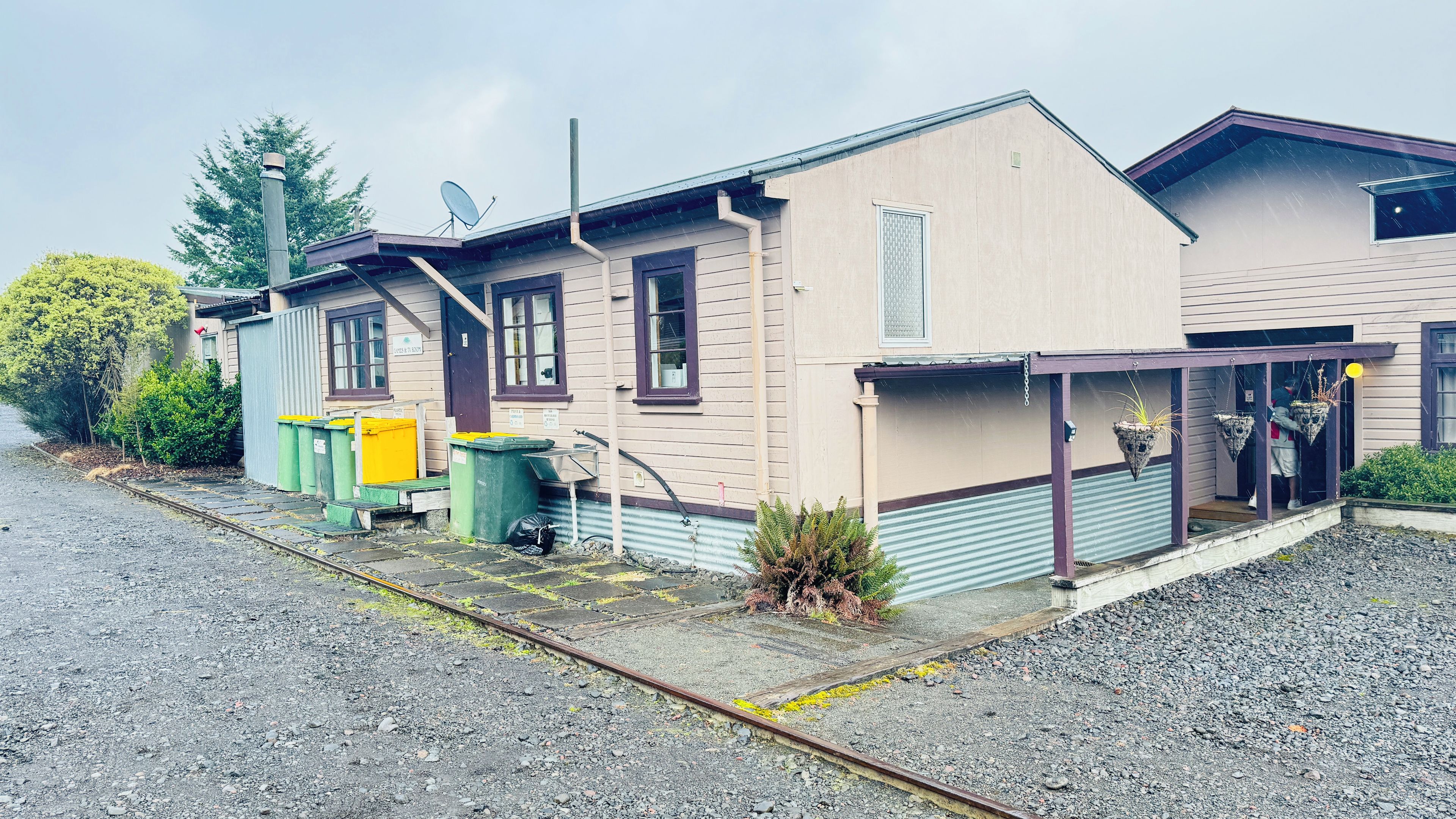 A building with a porch, a satellite dish, and a row of green and yellow dumpsters.