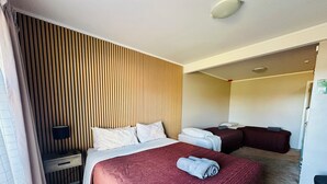 Habitación de hotel con una cama grande, una cama más pequeña, un escritorio, una lámpara y una pared con listones de madera verticales.