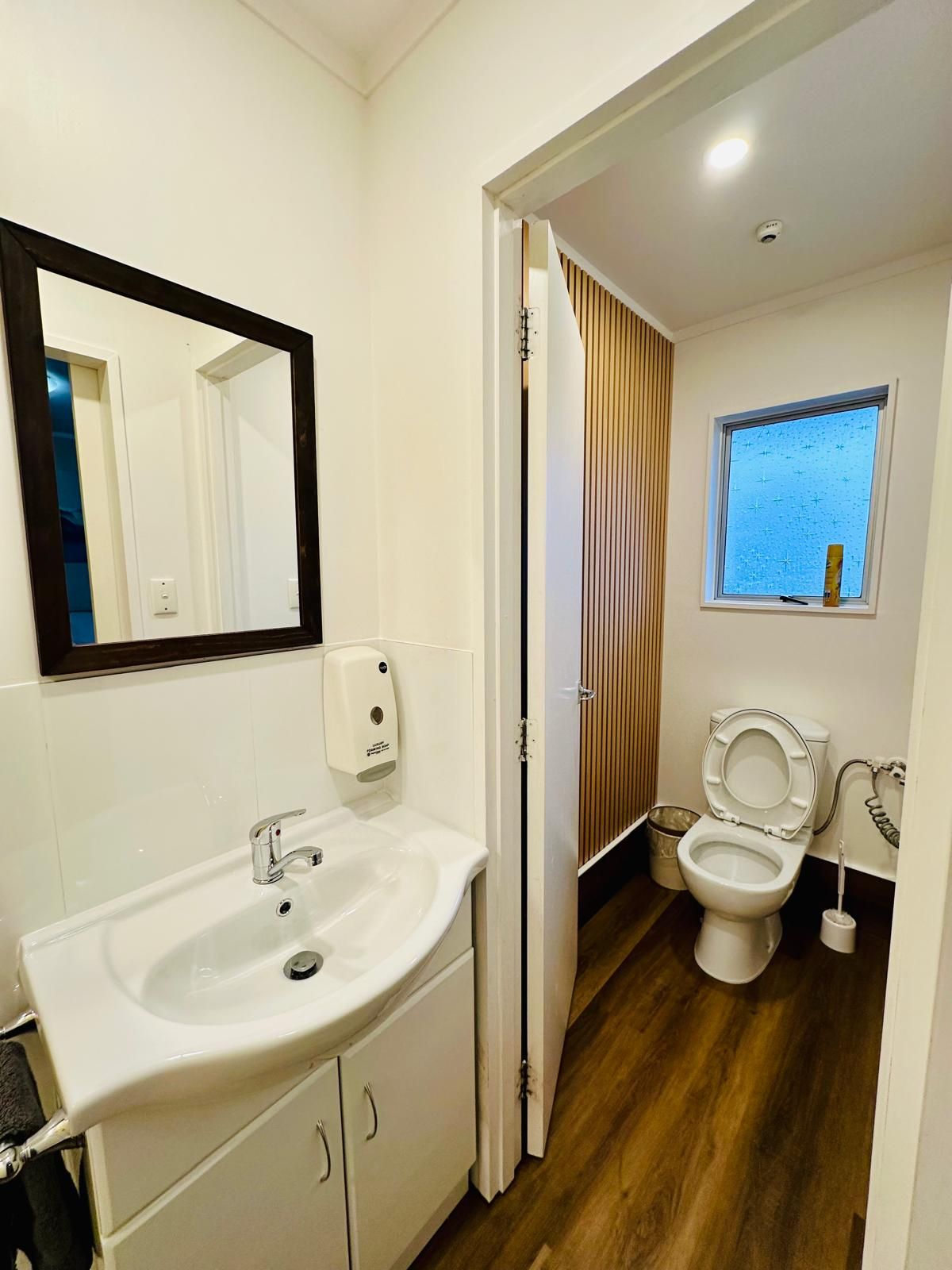 Un baño moderno con lavamanos, espejo y retrete blancos.