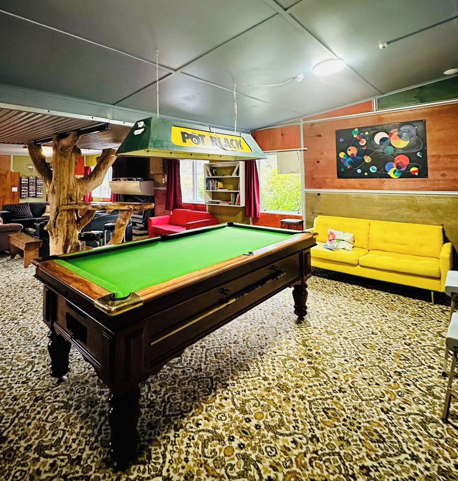 Ein Billardtisch in einem Raum mit Teppichmuster, einem gelben Sofa und einem Gemälde an der Wand.