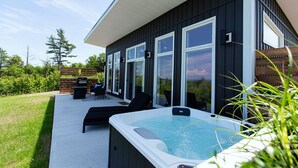 Una casa moderna con jacuzzi, mobiliario exterior y vistas al entorno verde.