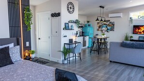 Una sala de estar moderna con un sofá, un comedor con mesa y sillas, una cocina con refrigerador azul y un televisor montado en la pared.