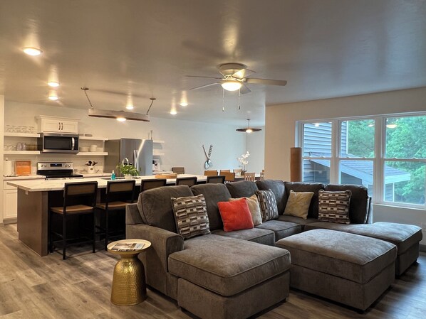 A modern kitchen with a built-in oven and microwave, a dining area with a large table and chairs, and a cozy seating area with a sectional sofa and ottomans.