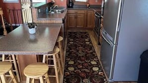 Una cocina con armarios de madera, un refrigerador de acero inoxidable, una isla central con taburetes y una alfombra estampada.