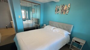 Un dormitorio con cama, mesita de noche, espejo y una pared decorada.