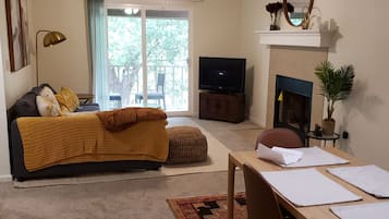 A living room with a sofa, a TV, a fireplace, a dining table with papers, and a ceiling fan.
