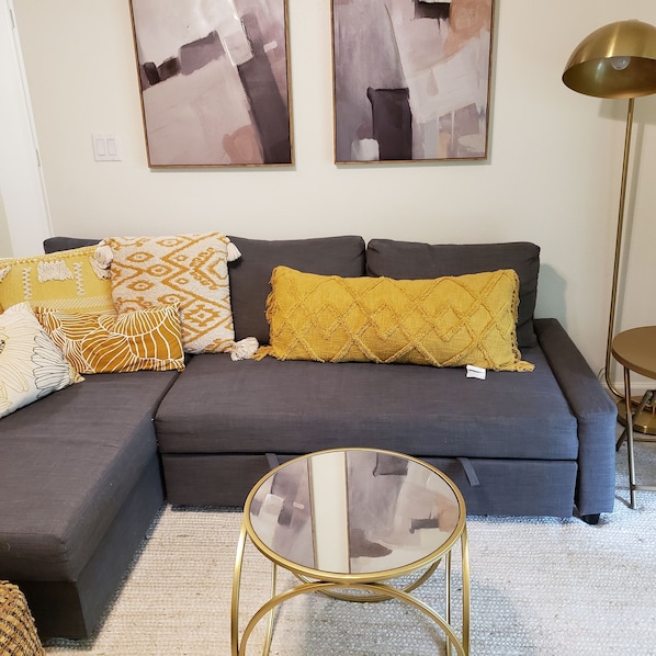 A modern living room with a grey sectional sofa, a glass coffee table, and decorative pillows.