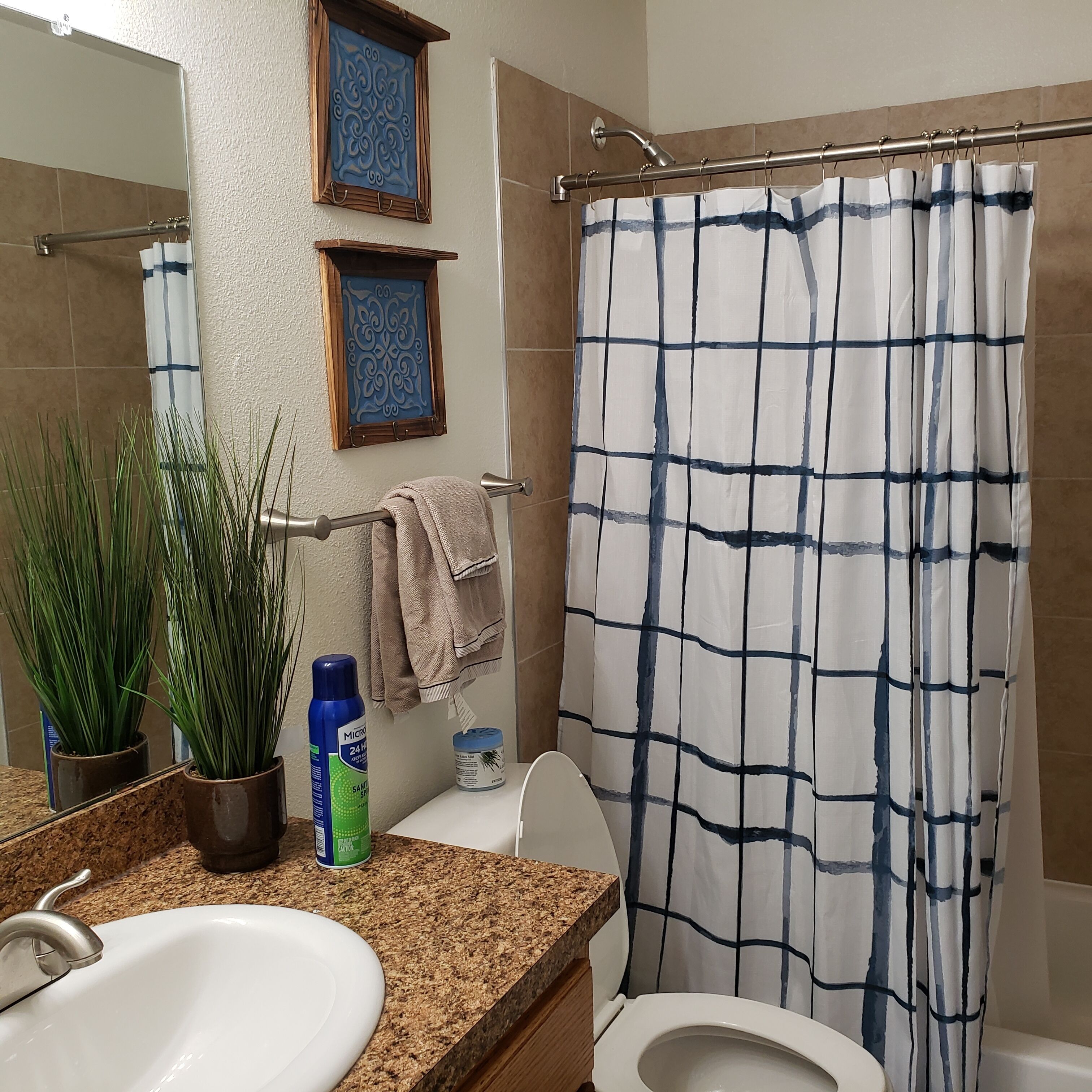 A bathroom with a sink, toilet, and shower curtain. There are decorative wall pieces above the sink and a towel hanging on the shower rod.