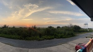 A sunset view from a covered outdoor area with a gravel path, a parked car, and a water tower in the background. - OCNJ Newly Renovated 4BR! (Ocean City)