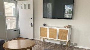 A living room with a grey sofa, a small round table, a white cabinet with wicker panels, and a mounted TV. - OCNJ Newly Renovated 4BR! (Ocean City)