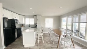 A modern kitchen with white cabinetry, a black refrigerator, and a wooden dining table with white chairs. - OCNJ Newly Renovated 4BR! (Ocean City)